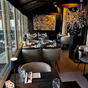 Elegant gedekte restauranttafels in een moderne ruimte met grote ramen, zwarte hanglampen en kleurrijke kunst aan de muur