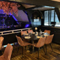 Ronde gedekte tafel met zes roze fluwelen stoelen in een sfeervol restaurant met zwarte hanglamp en roze bloesemdecoratie