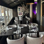Lange gedekte tafel met grijze boucl&eacute; stoelen in een sfeervol restaurant met zwarte hanglamp en witte bloesemdecoratie