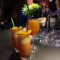 Drie oranje cocktails op de bar: twee gelaagde longdrinks met sinaasappel en rietjes, en &eacute;&eacute;n wijnglas met oranje drank
