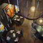 Bovenaanzicht van het sfeervolle restaurant met gedekte tafels, designer hanglampen en kleurrijke kunst aan de donkere muur