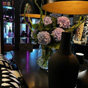 Stijlvolle tafelsetting met een grote vaas paarse hortensia&rsquo;s, zwarte decoratieve vazen en moderne zwarte hanglampen met warm licht
